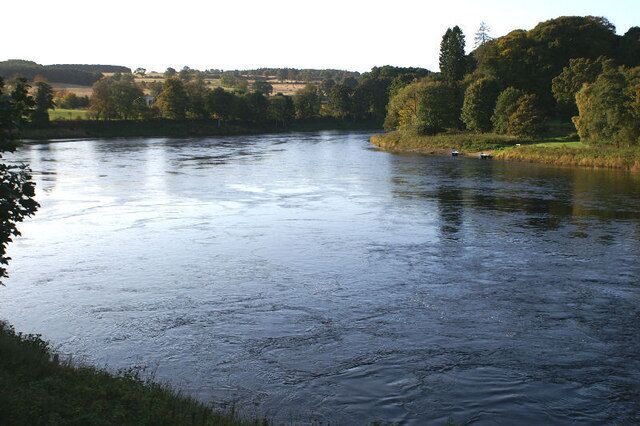 A river with calm waters, surrounded by trees and grassy banks.