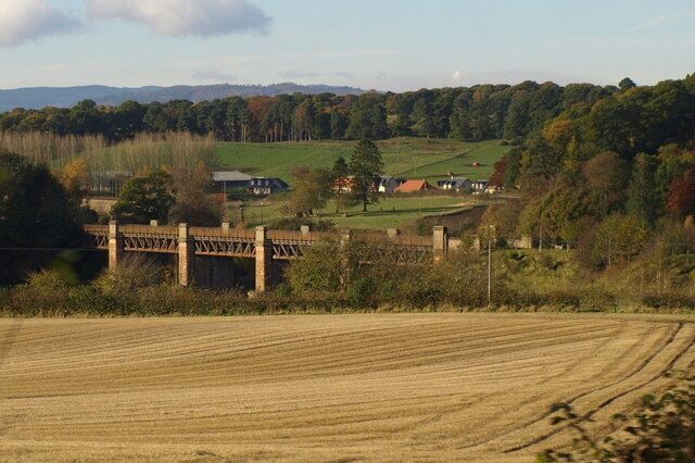 A rural landscape with a bridge, fields, and houses in the distance.