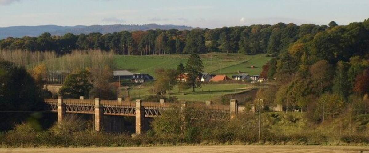 A rural landscape with a bridge, fields, and houses in the distance.