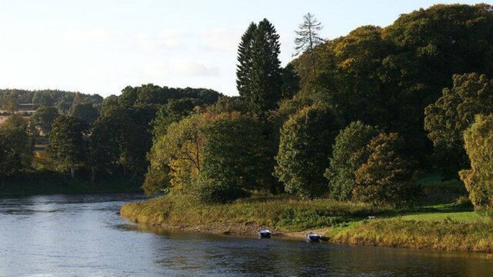 A river with boats, surrounded by dense forest and hills.