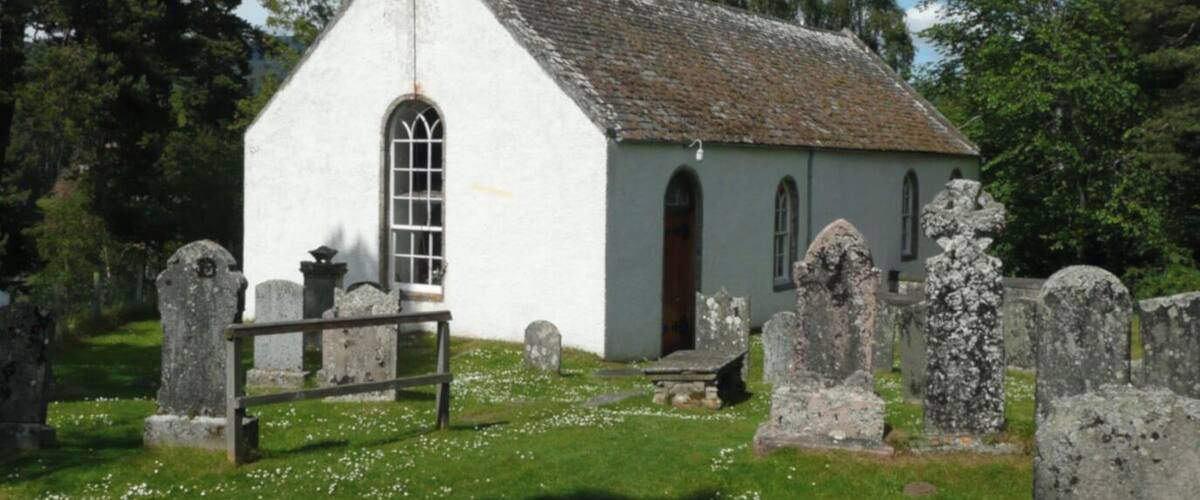 A small white church with a bell tower, surrounded by a cemetery with headstones.