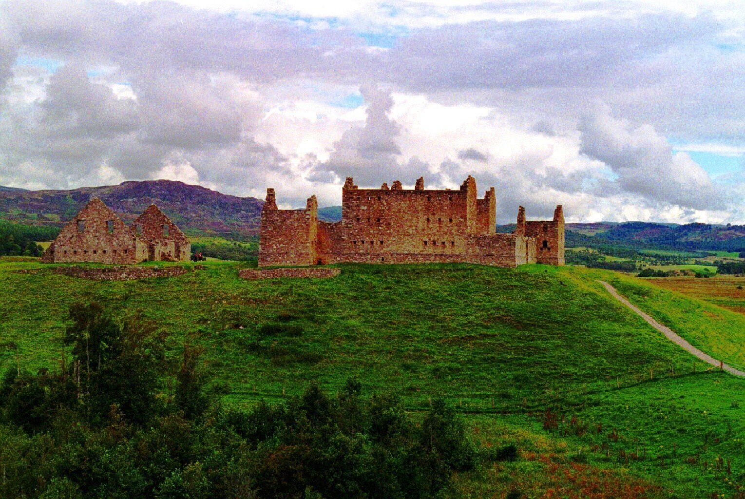 A historic castle with ruins and a lush green field.