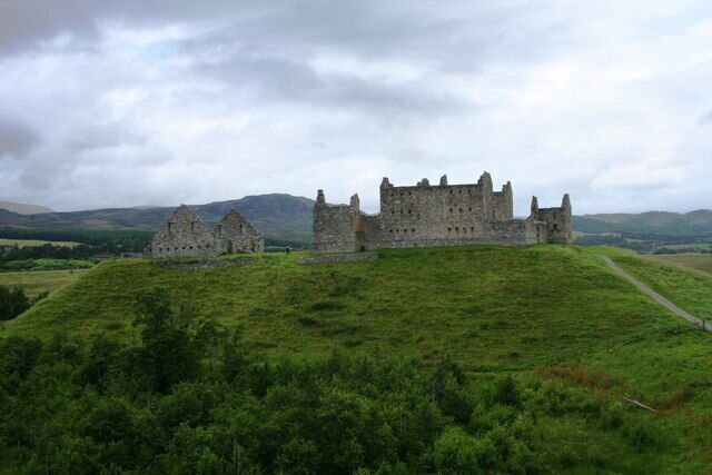 A historic castle on a grassy hill with a cloudy sky.
