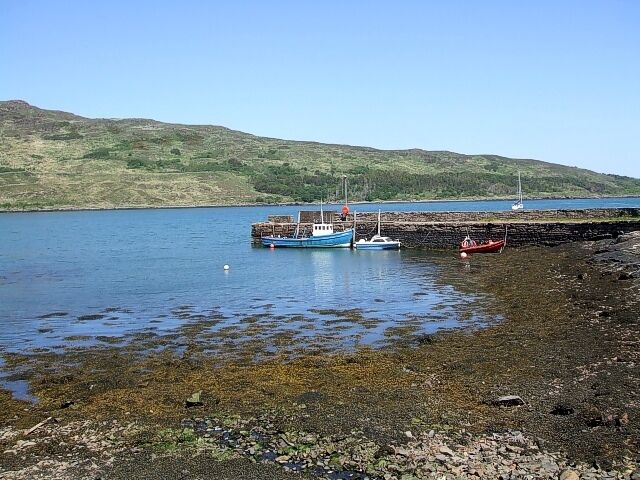 A calm lake with boats, rocky shore, and hills in the background.