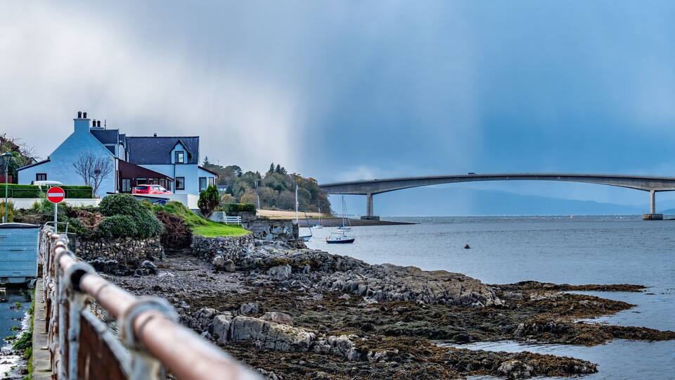 A coastal town with a bridge over the water, a lighthouse, and rocky shores.