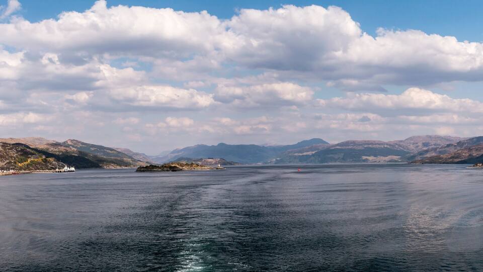 A calm lake with mountains in the background and a few boats on the water.