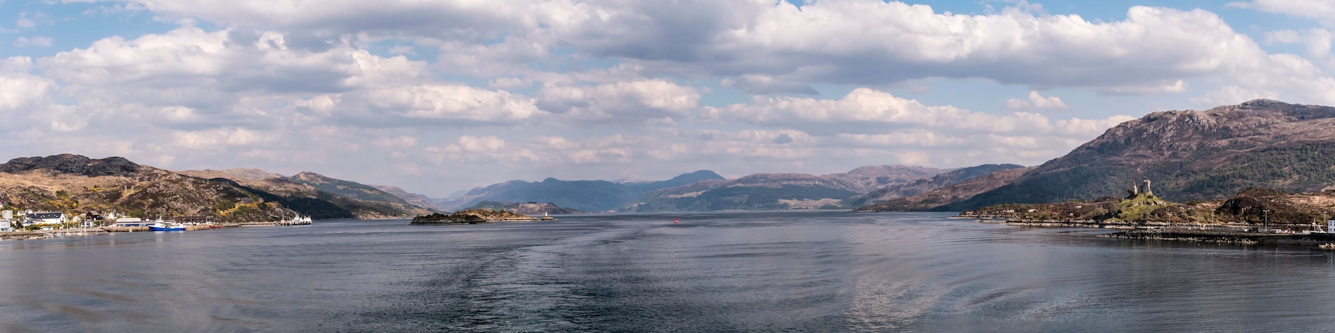 A calm lake with mountains in the background and a few boats on the water.