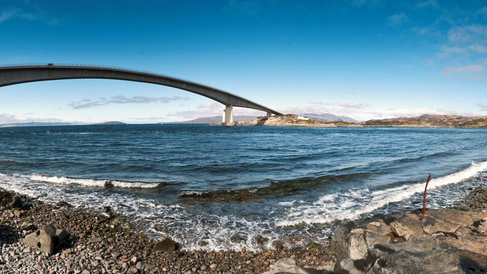 A coastal bridge over a rocky shoreline with waves crashing onto the beach.