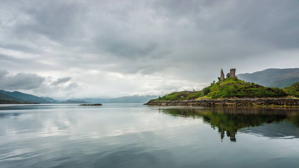 A calm lake with a rocky island featuring ancient ruins and lush greenery.