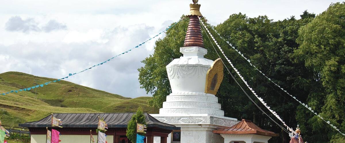 A white stupa with a golden top, surrounded by prayer flags and a small shrine.