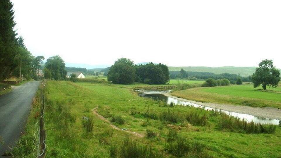 A rural landscape with a narrow road, a small stream, and green fields.