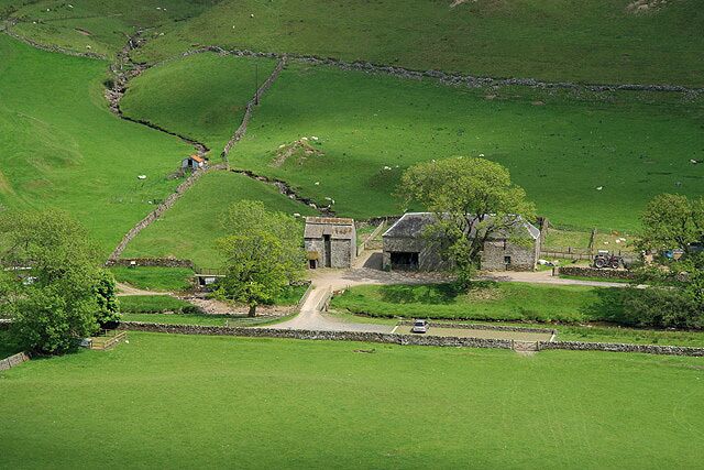 A rural landscape with a stone house, green fields, and a stone wall.