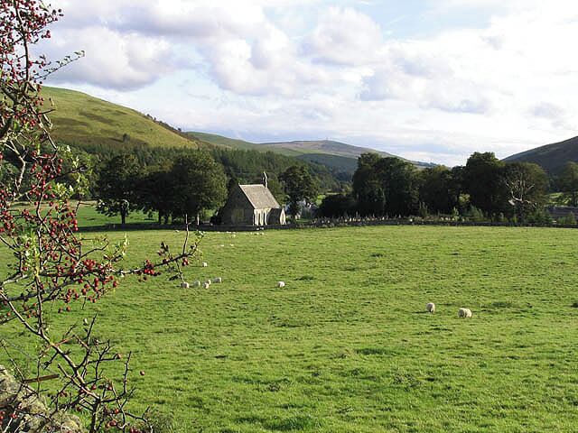 A green field with sheep, a small house, and trees in a hilly landscape.