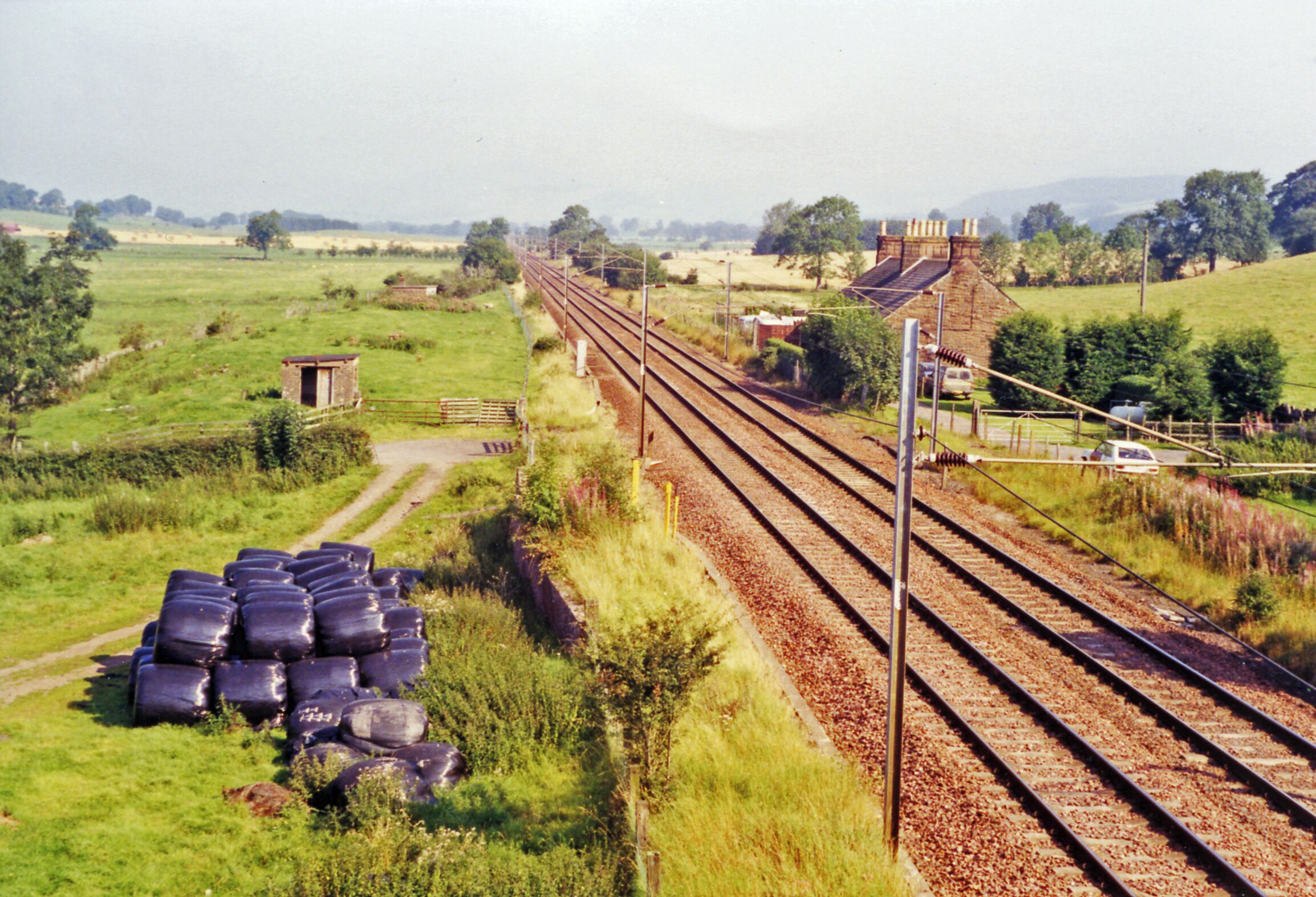 A rural railway track with multiple lines, surrounded by green fields and a small building.