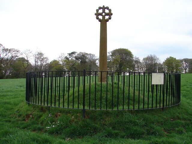 A tall, cylindrical monument with a star-like top, surrounded by a black metal fence in a grassy field.