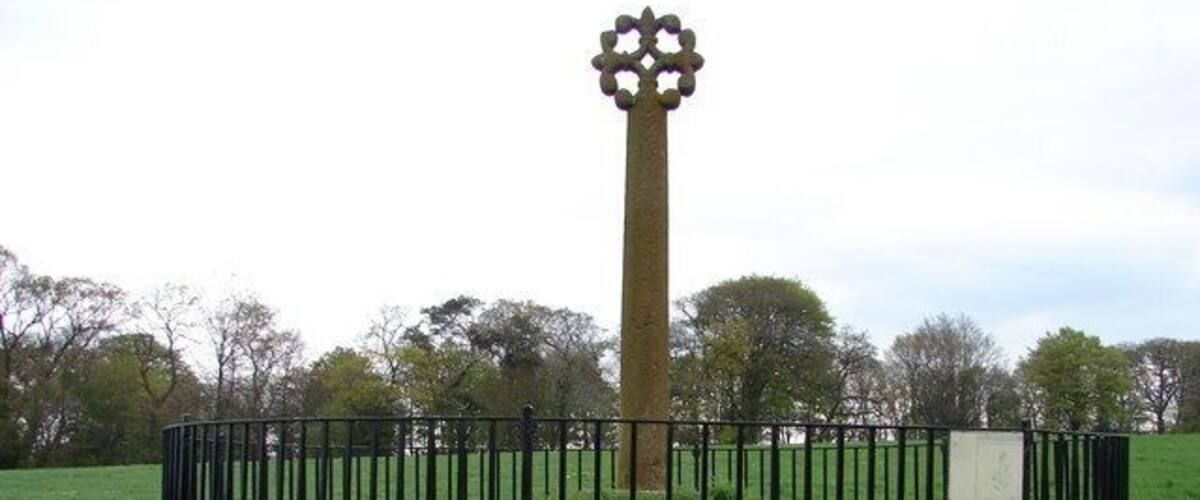 A tall, cylindrical monument with a star-like top, surrounded by a black metal fence in a grassy field.