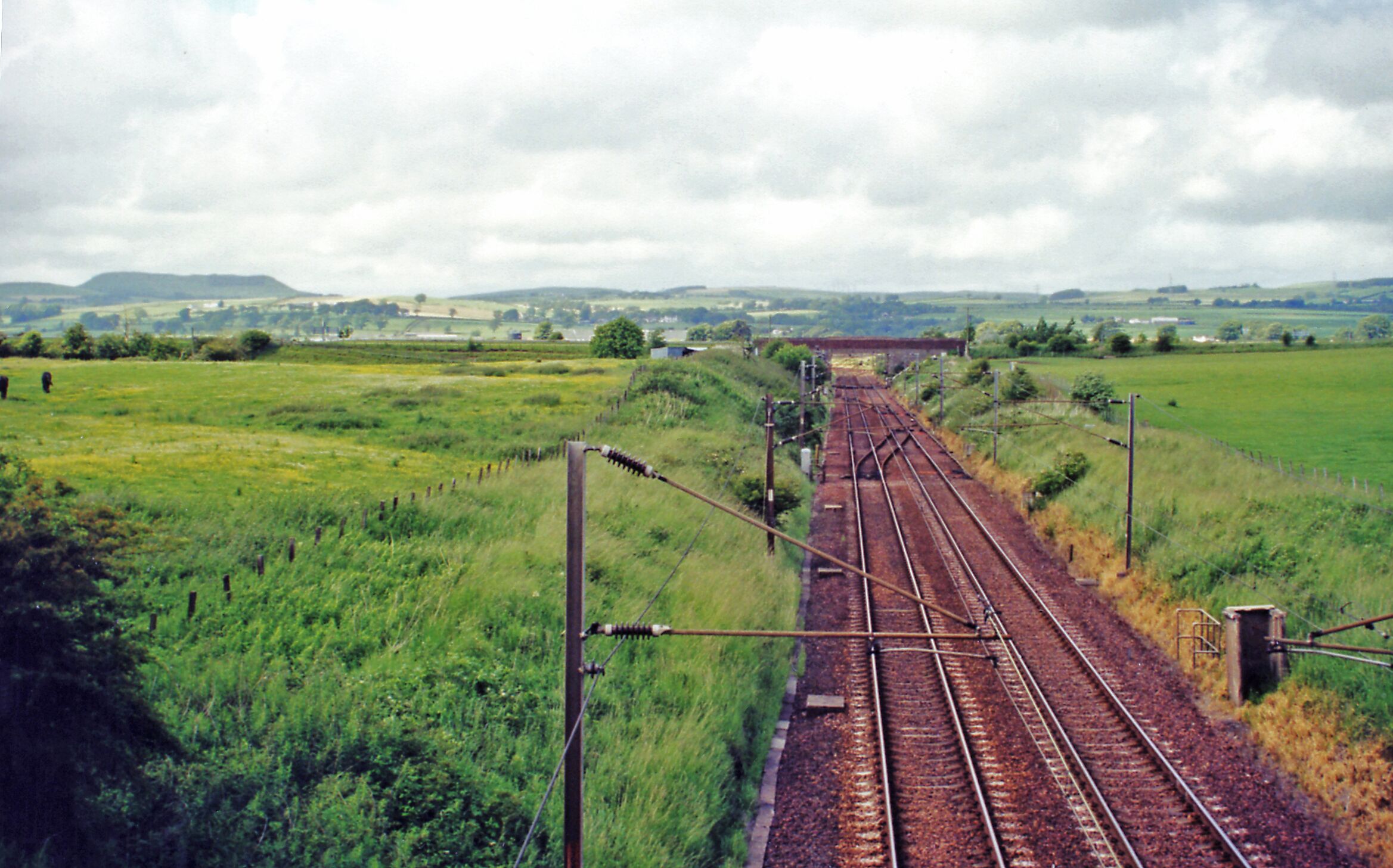 Down the West Coast Main Line at Kirtlebridge. View NW from B722 bridge, towards Beattock Summit, Carstairs and Glasgow/Edinburgh: ex-Caledonian Railway (Carlisle - Glasgow/Edinburgh) section of the WCML, electrified 1974. The view is up the Annan Valley and the peak on the left horizon may be Queensberry (2,285 ft.) in the Lowther Hills [?]