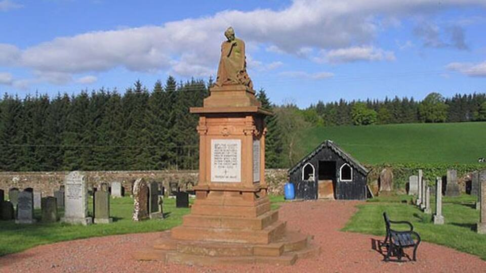 A cemetery with a central monument, a small building, and a bench.