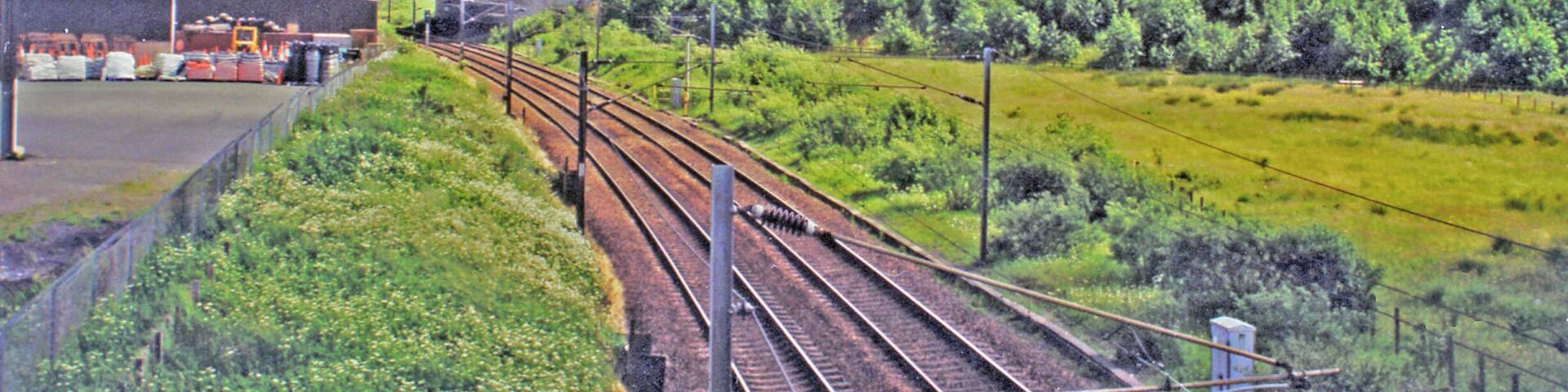 Site of former Kirtlebridge station, WCML 2000. View southward from B722 to the large bridge of the new A74(M). This is situated where the station had been, until it closed 13/6/60 to passengers (6/4/64 to goods). The view is up the ex-Caledonian Railway (Glasgow - Carlisle) section of the West Coast Main Line, electrified 1974. Off to the right used to be the branch line to Annan (Shawhill) and over the Solway Viaduct to Brayton on the Maryport & Carlisle Railway; this lasted to Brayton only until 20/5/21, to Annan for passengers until 27/4/31 (goods 28/2/55, however).