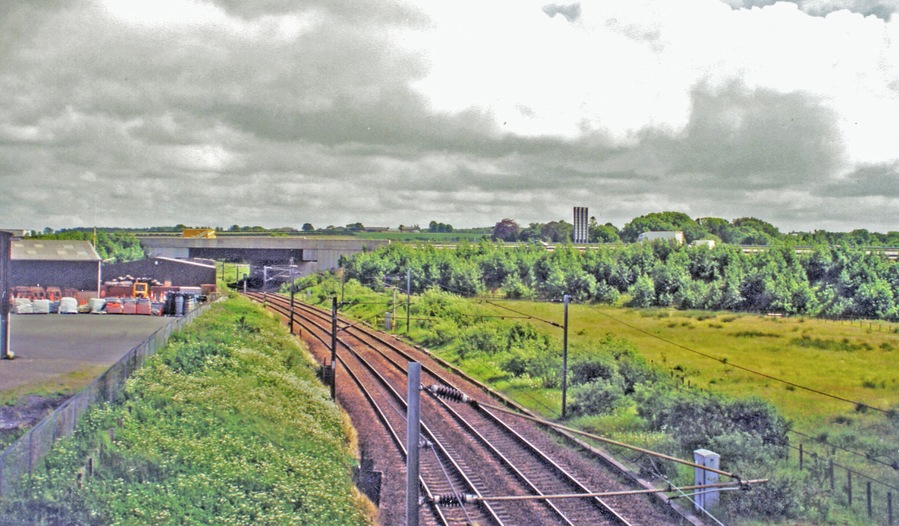 Site of former Kirtlebridge station, WCML 2000. View southward from B722 to the large bridge of the new A74(M). This is situated where the station had been, until it closed 13/6/60 to passengers (6/4/64 to goods). The view is up the ex-Caledonian Railway (Glasgow - Carlisle) section of the West Coast Main Line, electrified 1974. Off to the right used to be the branch line to Annan (Shawhill) and over the Solway Viaduct to Brayton on the Maryport & Carlisle Railway; this lasted to Brayton only until 20/5/21, to Annan for passengers until 27/4/31 (goods 28/2/55, however).