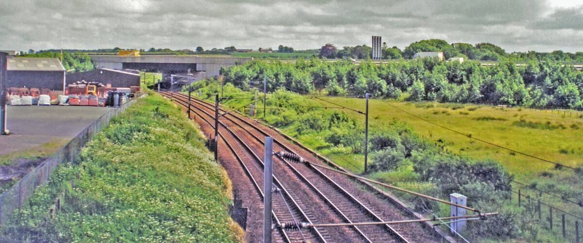 Railway tracks, a building, and a green field with trees.