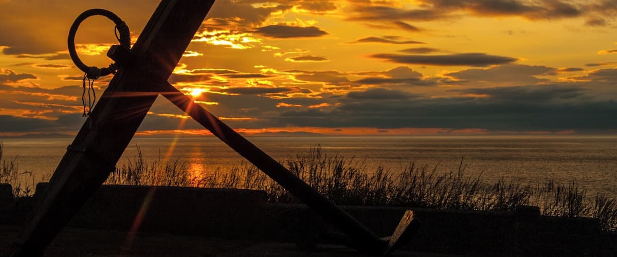 A sunset over a body of water with a sailboat and a ring buoy in the foreground.