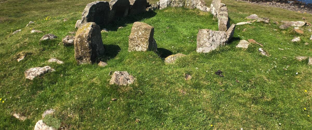 A grassy area with stone structures and a body of water in the background.