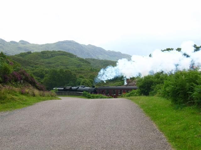 A train on a rural road with hills in the background.