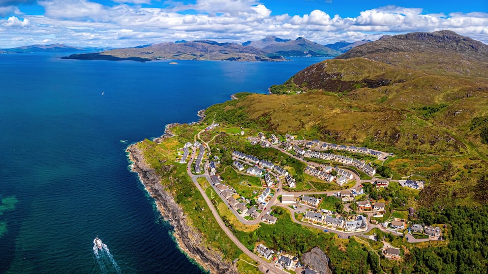 An aerial view of a coastal town with a marina, surrounded by mountains and a large body of water.
