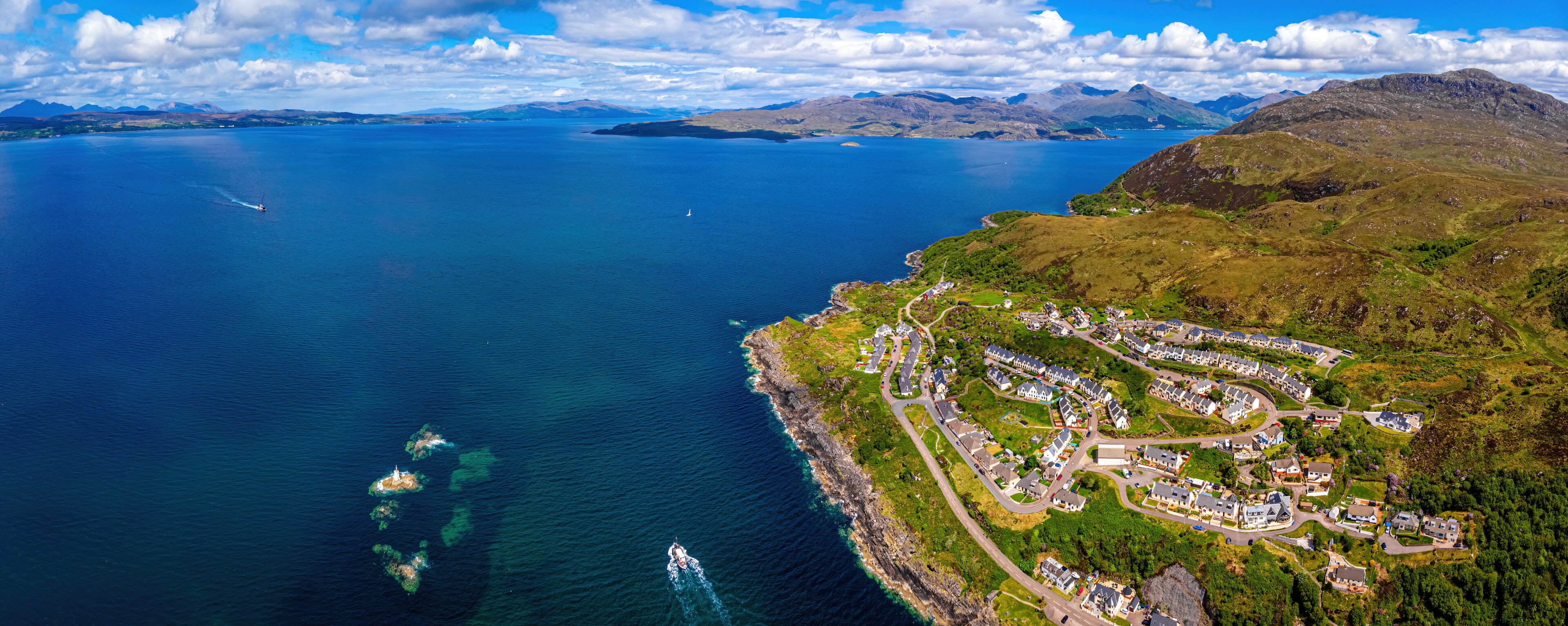 An aerial view of a coastal town with a marina, surrounded by mountains and a large body of water.