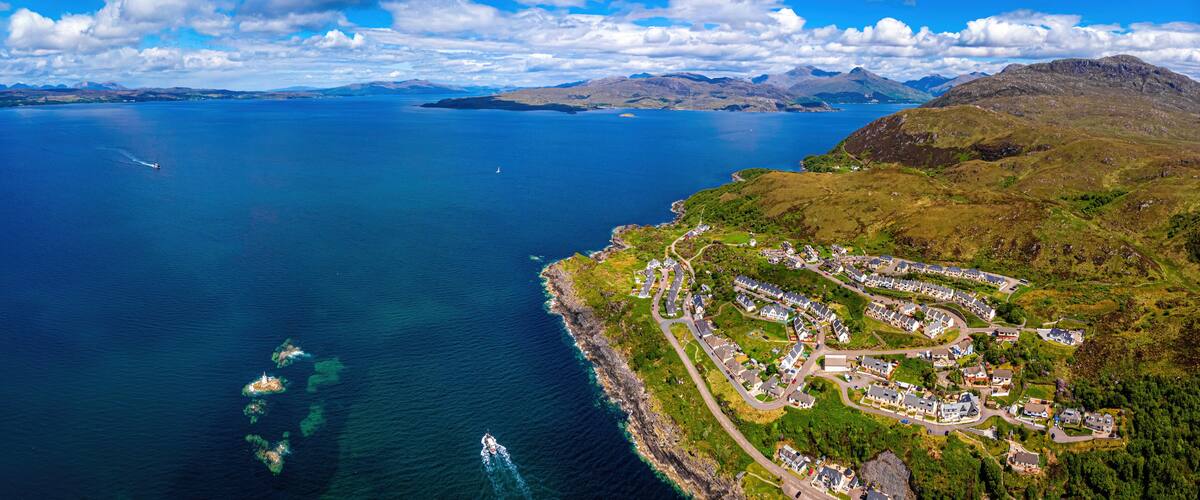 An aerial view of a coastal town with a marina, surrounded by mountains and a large body of water.