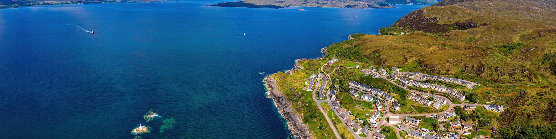 An aerial view of a coastal town with a marina, surrounded by mountains and a large body of water.
