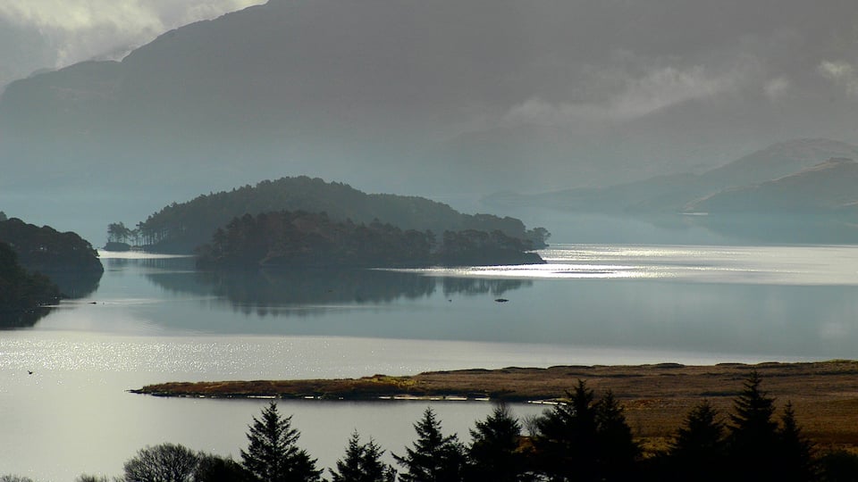 A calm lake with a small island in the center, surrounded by mountains and trees.