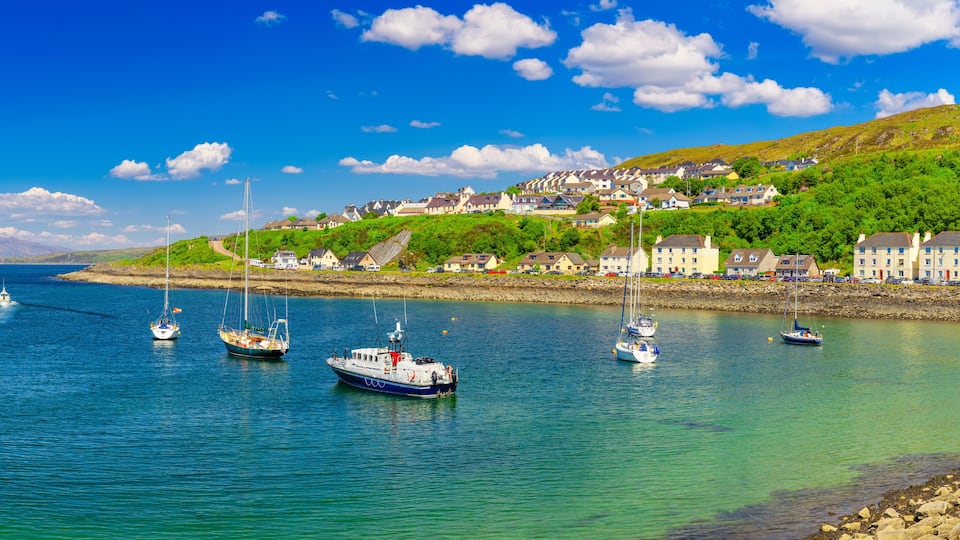 A coastal town with houses on a hillside, boats on the water, and a clear blue sky.
