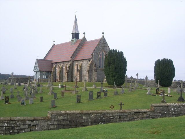 A church with a red roof and stone walls, surrounded by a cemetery with numerous gravestones.