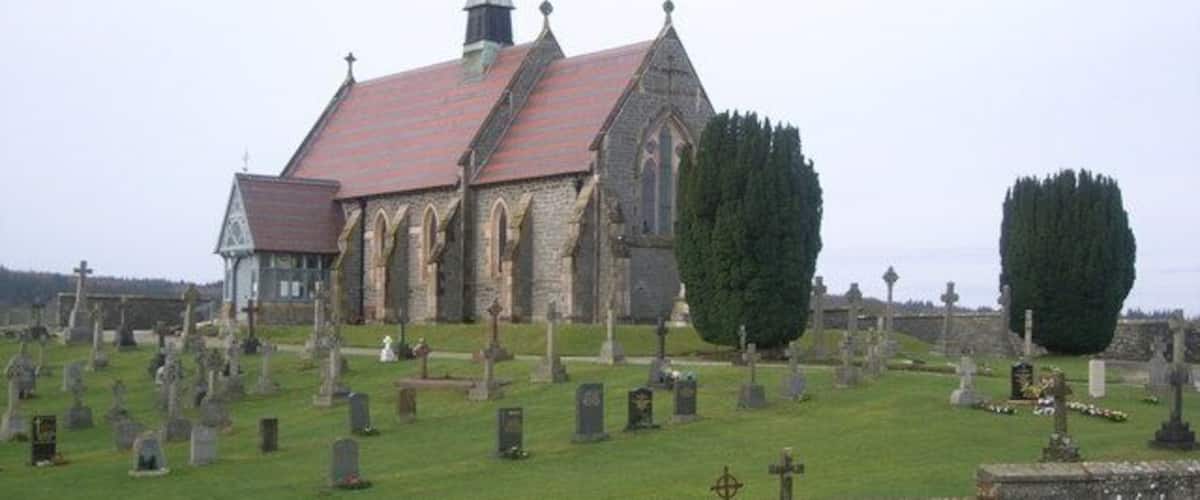 A church with a red roof and stone walls, surrounded by a cemetery with numerous gravestones.