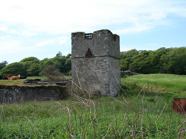 Uma torre de pedra em um campo gramado com árvores ao fundo.