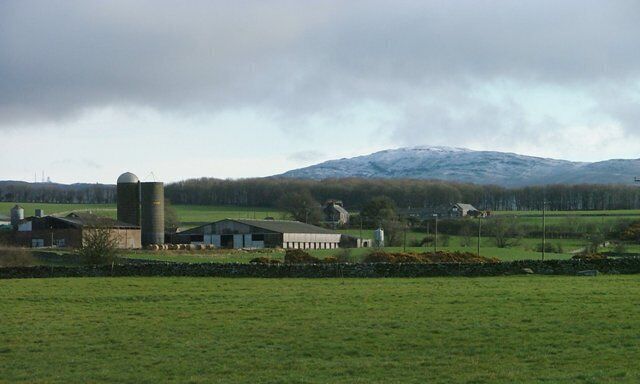 A rural landscape with a farm, a silo, and a mountain in the background.