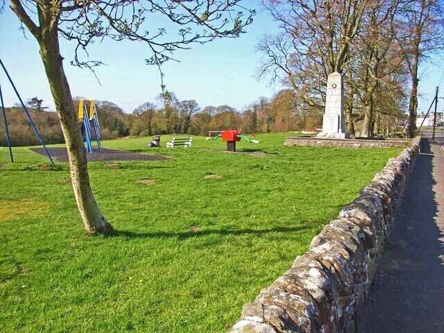 A park with a stone wall, a monument, and playground equipment.
