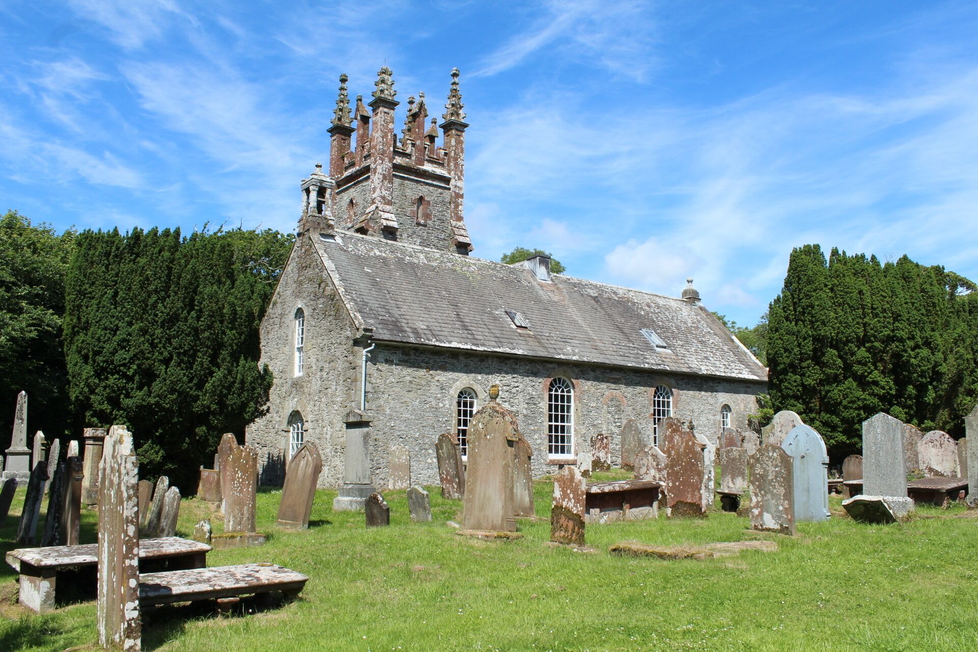 A historic church with a tall tower and multiple spires, surrounded by a cemetery with numerous gravestones.