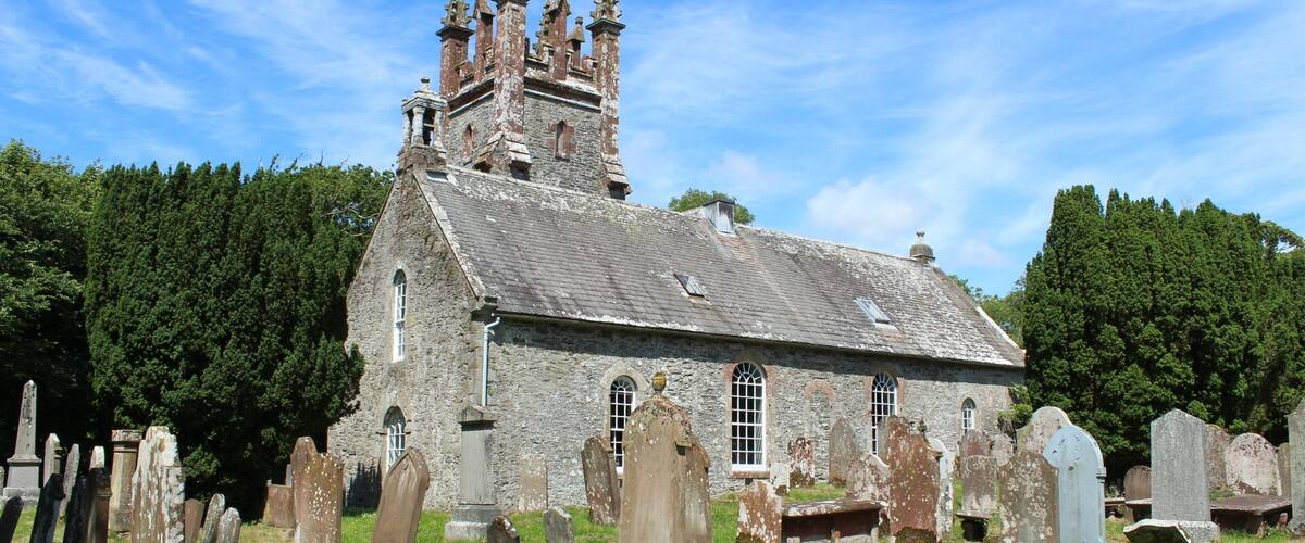 A historic church with a tall tower and multiple spires, surrounded by a cemetery with numerous gravestones.