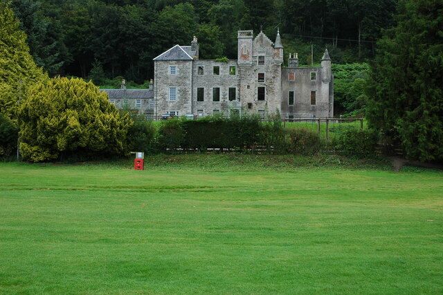 A large, historic stone building with multiple towers and a well-maintained lawn in the foreground.