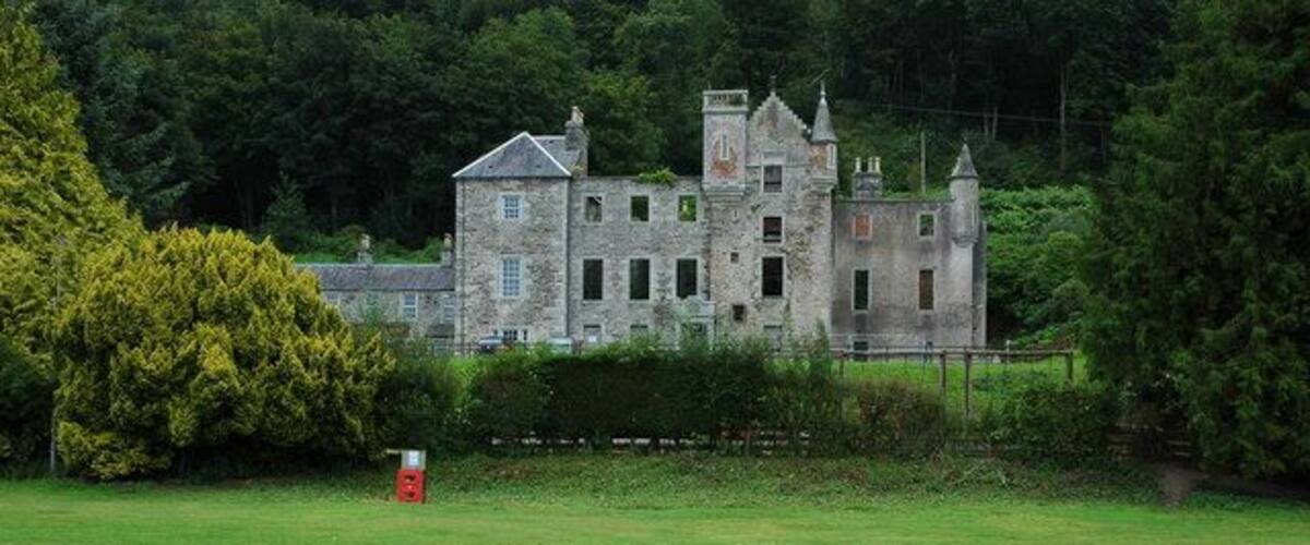 A large, historic stone building with multiple towers and a well-maintained lawn in the foreground.