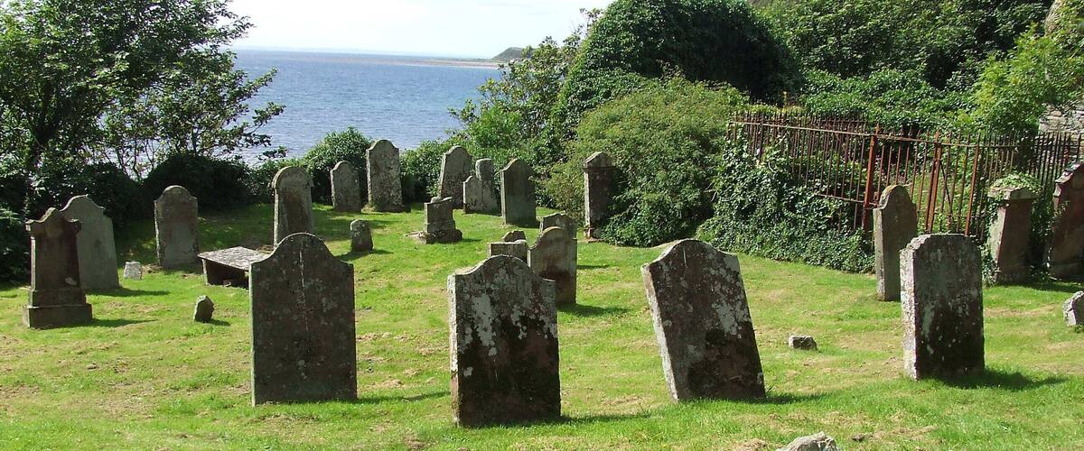 A coastal cemetery with stone headstones and a metal fence.