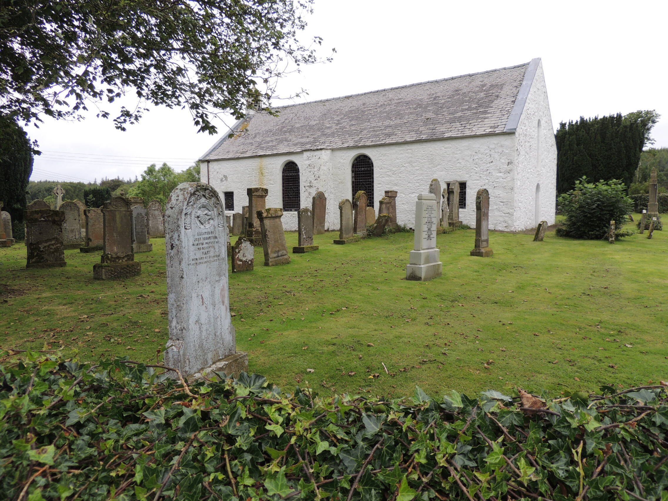 A white church with a steep roof surrounded by gravestones in a cemetery.