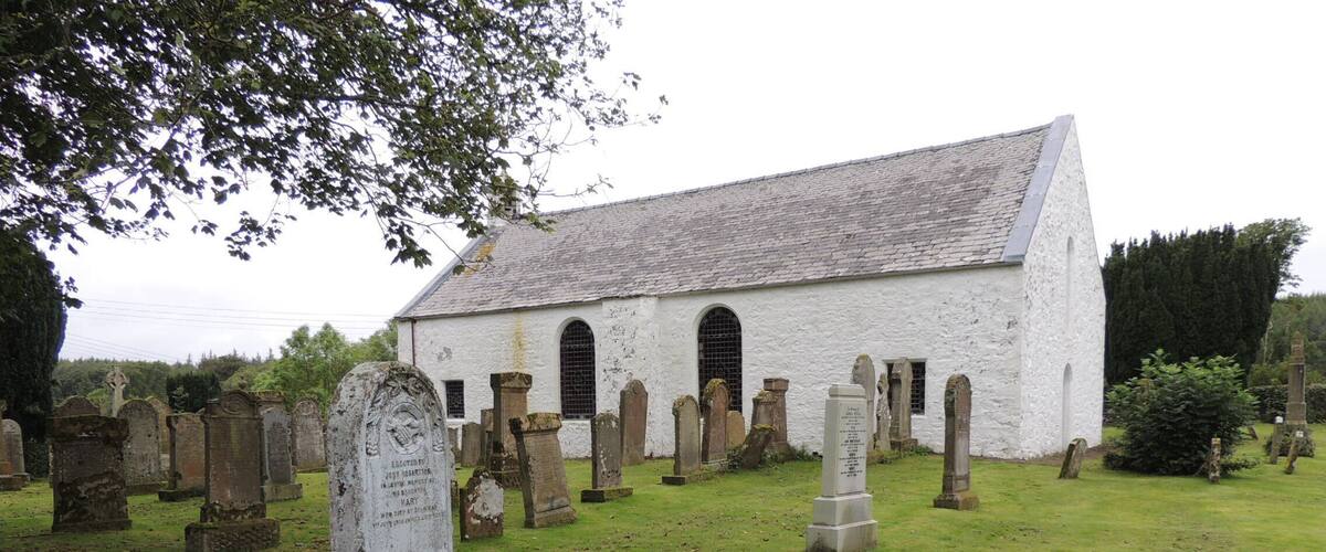 A white church with a steep roof surrounded by gravestones in a cemetery.