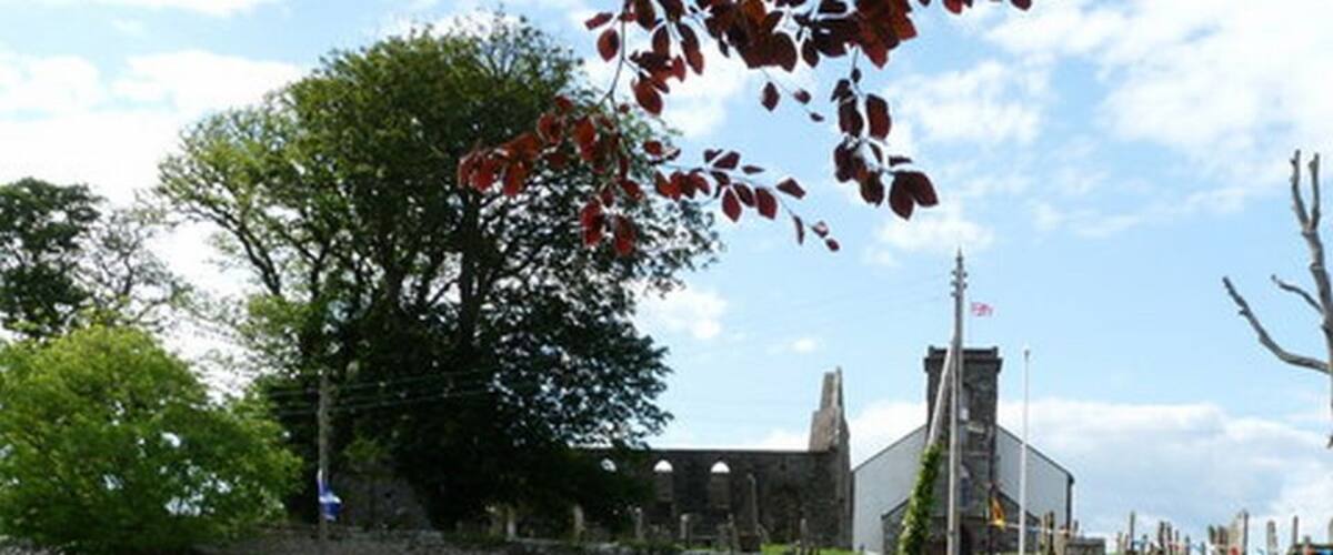 A grassy area with picnic tables, a stone wall, and a building with a flagpole.