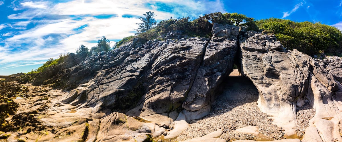 A rocky coastline with a narrow passage between large boulders, a sandy beach, and sparse vegetation.