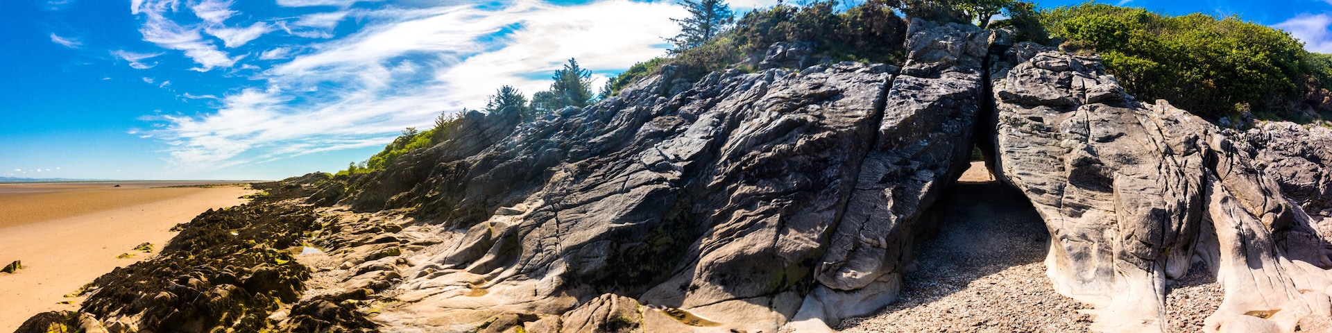 A rocky coastline with a narrow passage between large boulders, a sandy beach, and sparse vegetation.