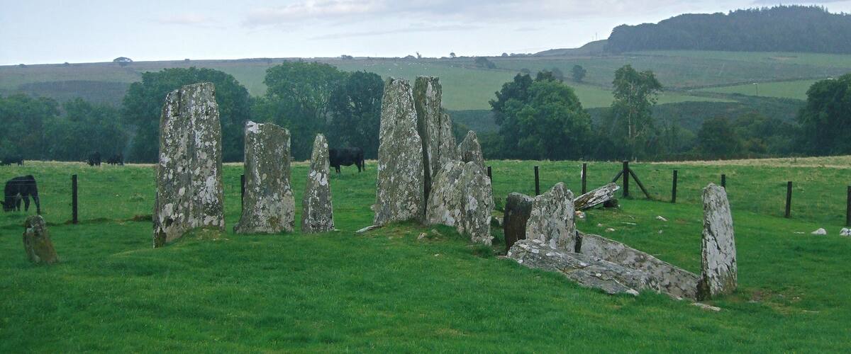 A stone circle in a grassy field with cows grazing in the background.